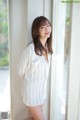 A woman standing in front of a window wearing a white shirt.