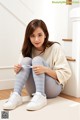 a woman sitting on the floor wearing a white sweater and blue striped tights