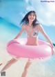 A woman in a bikini holding an inflatable ring on the beach.