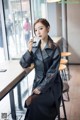 A woman in a black leather trench coat sitting at a table.