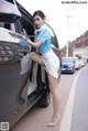 A woman in a blue shirt and white skirt getting out of a car.