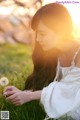 A woman in a white dress sitting in the grass with a dandelion.