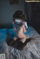 A naked woman sitting on a bed wearing a virtual reality headset.